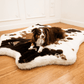 Dog lying on a cowhide rug in a room with wooden flooring and white walls.