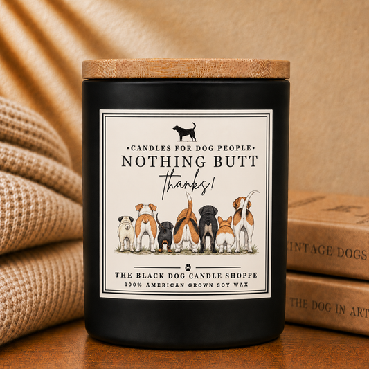 A black soy wax candle jar with a natural wood lid sits on a wooden surface next to a beige burlap blanket and stacked vintage dog books. The front label features an illustration of various dog breeds with the text 'Candles for Dog People.