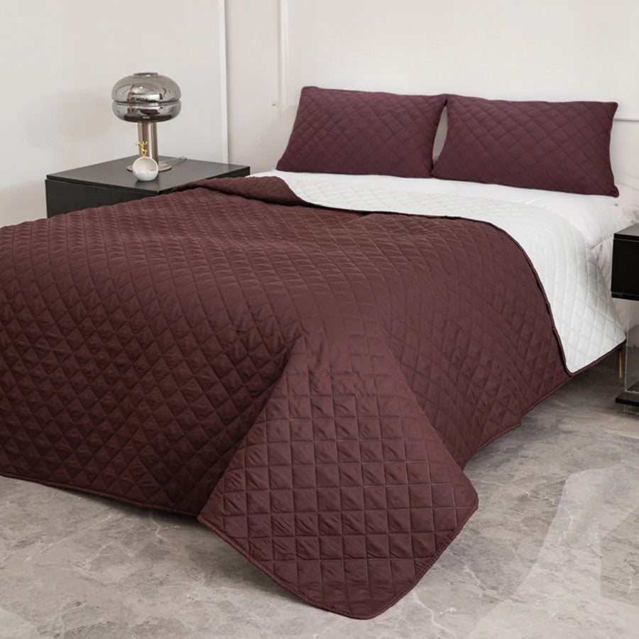 Maroon quilted coverlet on a bed with matching pillows in a bedroom setting.