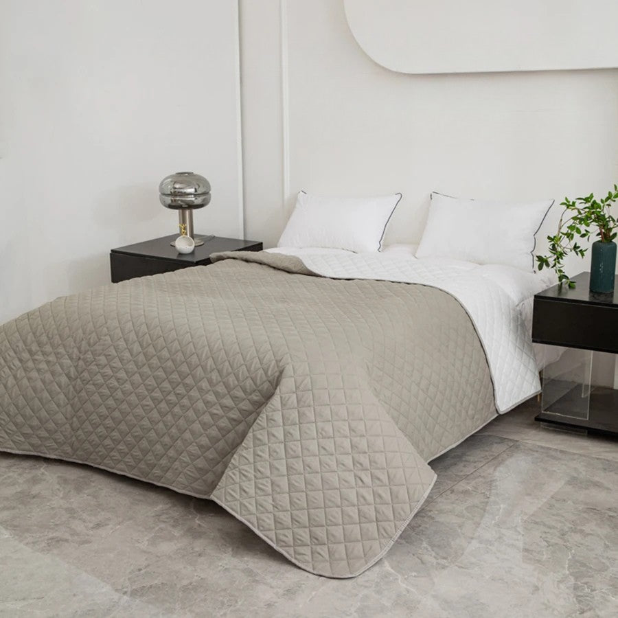 Bed with a gray quilt and white pillows in a modern bedroom setting.