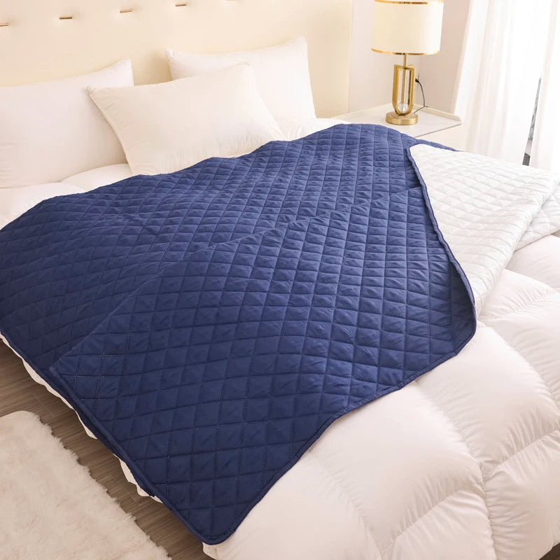 Blue quilted blanket on a bed with white bedding and pillows.